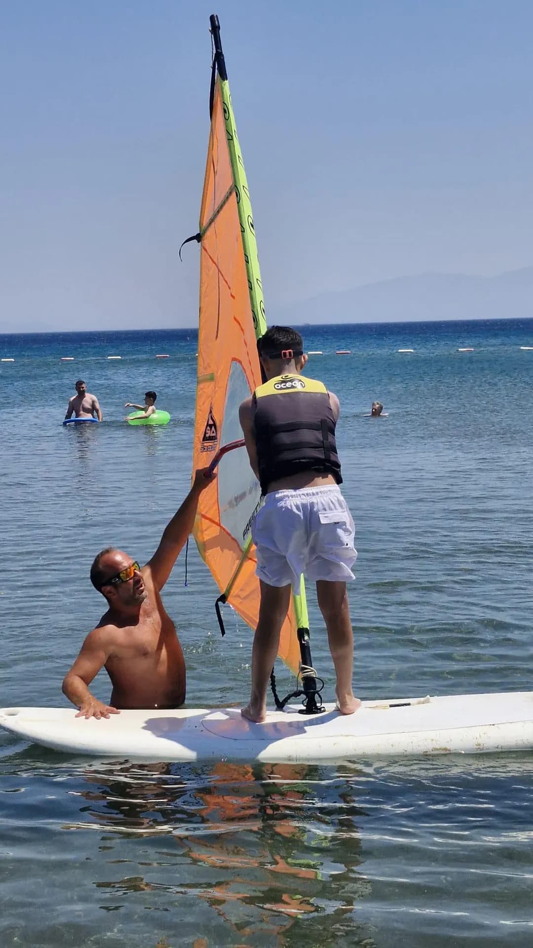 Vela'da eğitmenle yelken kontrolü çalışan windsurf katılımcısı