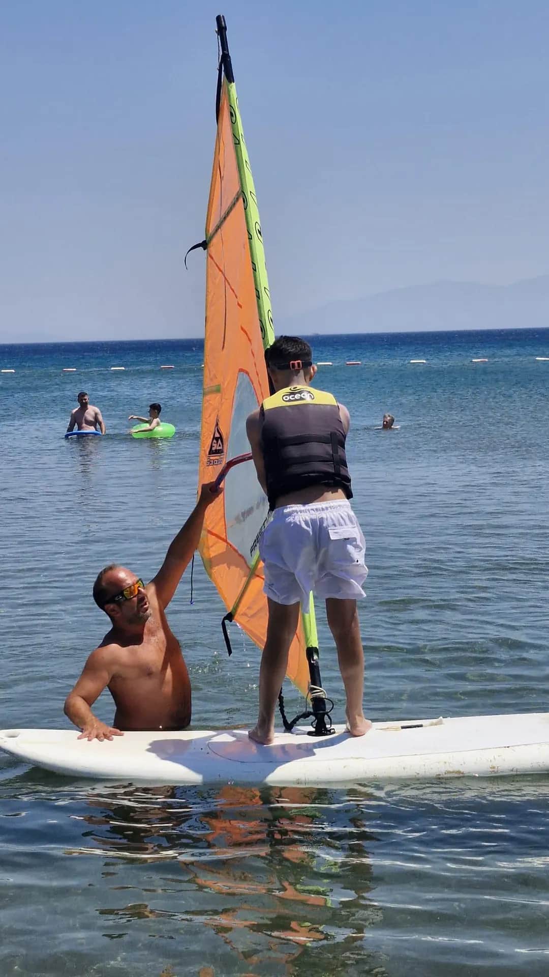 Vela'da board üzerindeki katılımcıya yelken kontrolü gösteren eğitmen